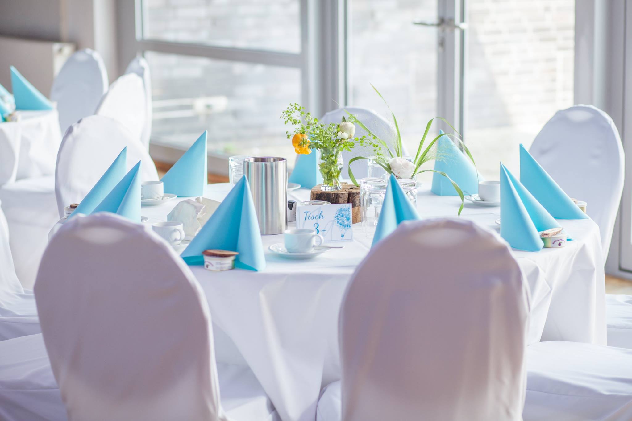Festlich gedeckter Tisch mit blauen Servietten und weißen Stuhlhussen