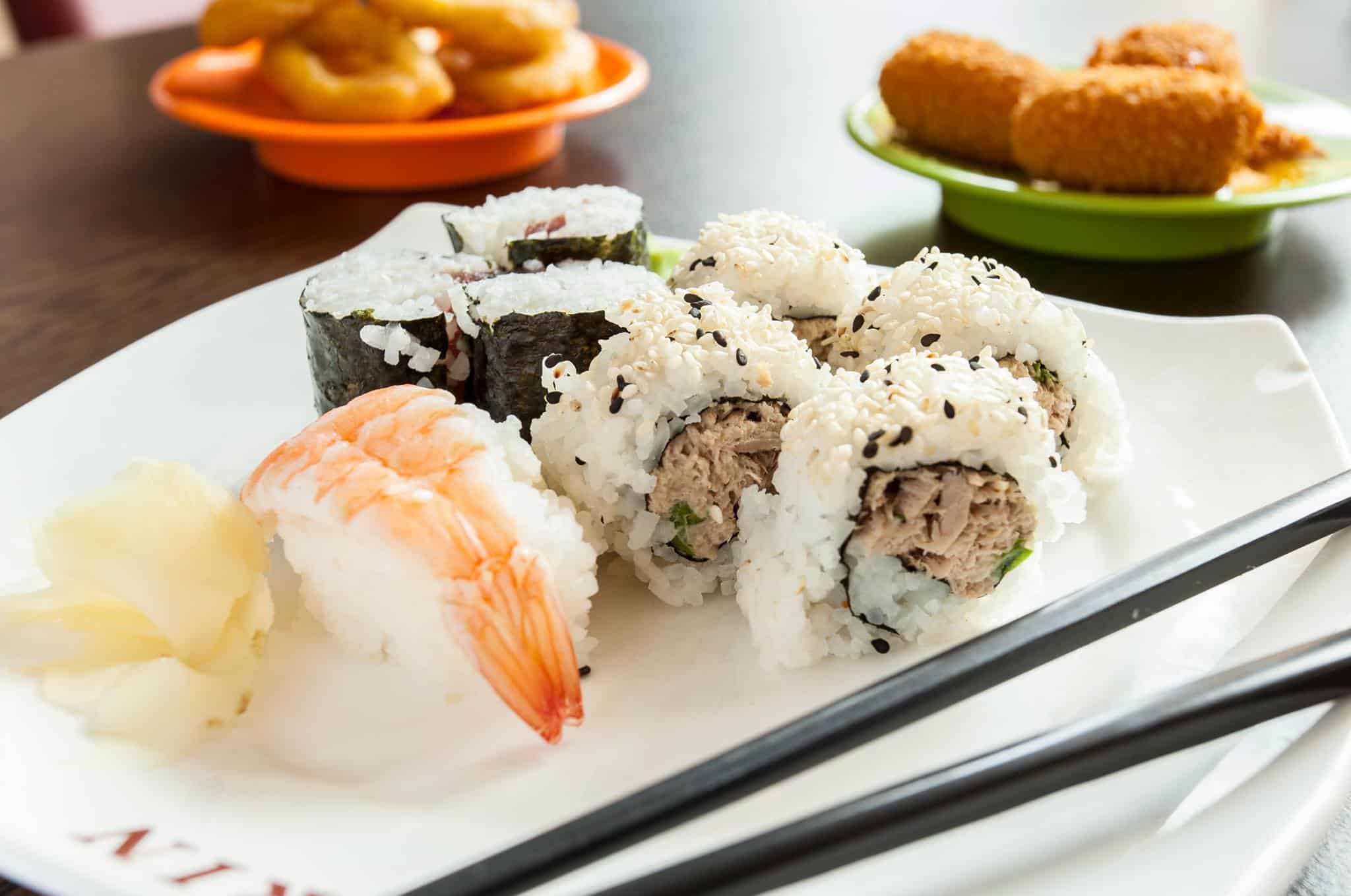 Teller mit Sushi, daneben Vorspeisen und Stäbchen