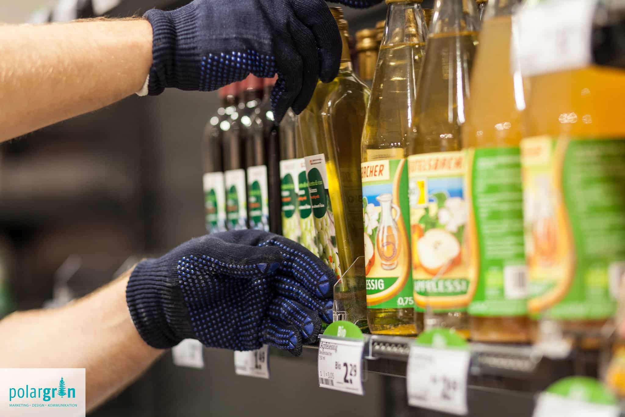 Hände mit Arbeitshandschuhen räumen Ölflaschen in ein Verkaufsregal