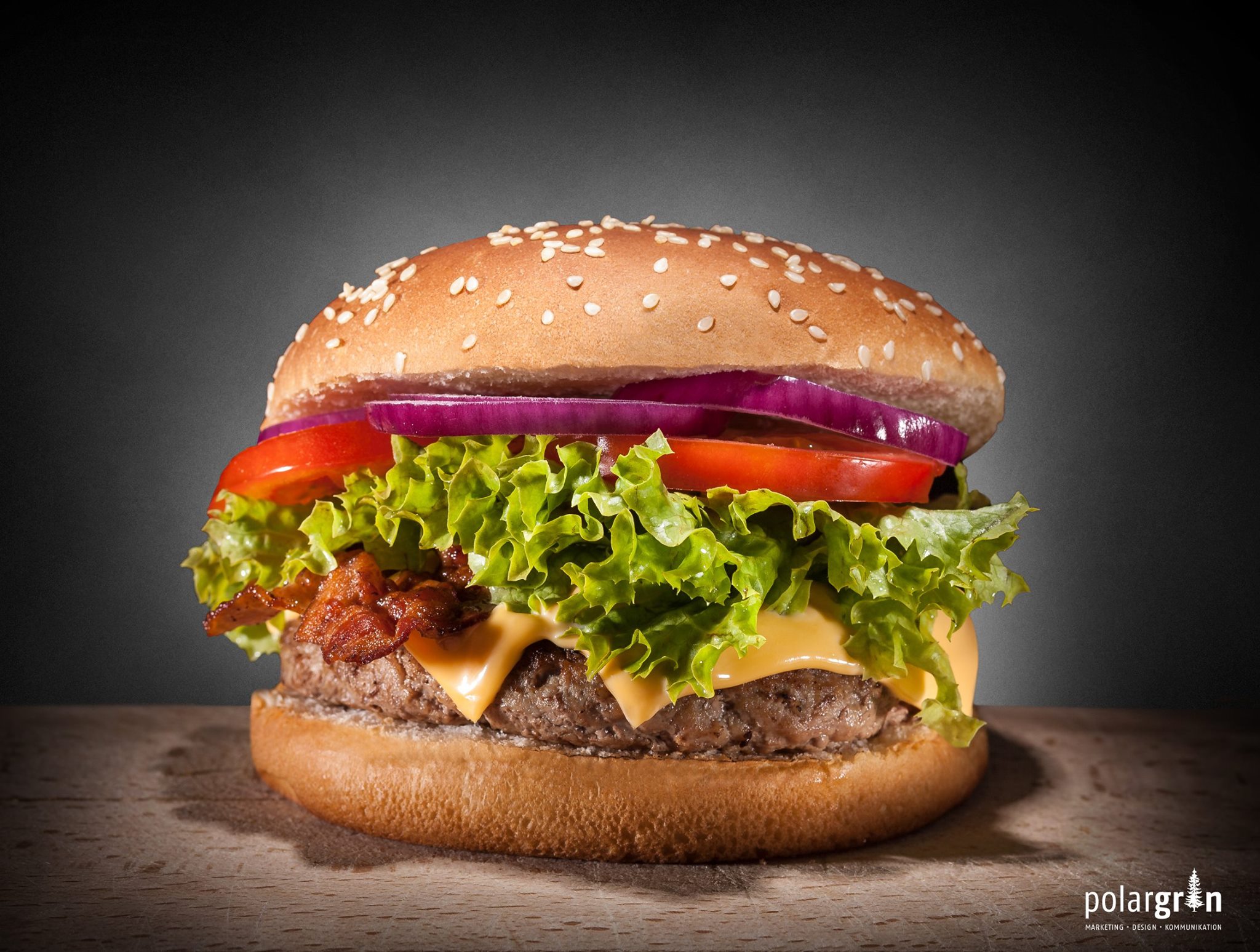 Produktaufnahme eines Burgers mit Salat, Tomate und Zwiebel vor dunklem Hintergrund