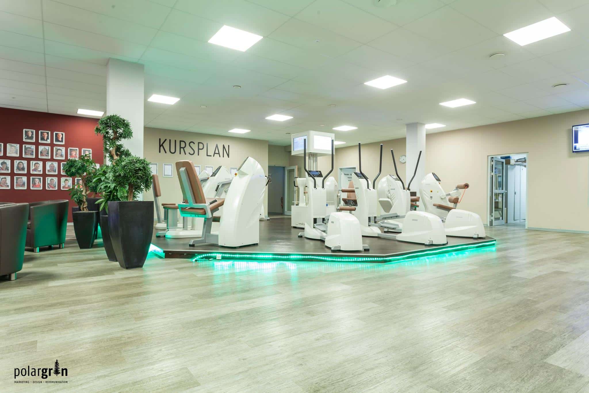 Fitnessstudio mit Trainingsgeräten und einer Tafel „Kursplan“