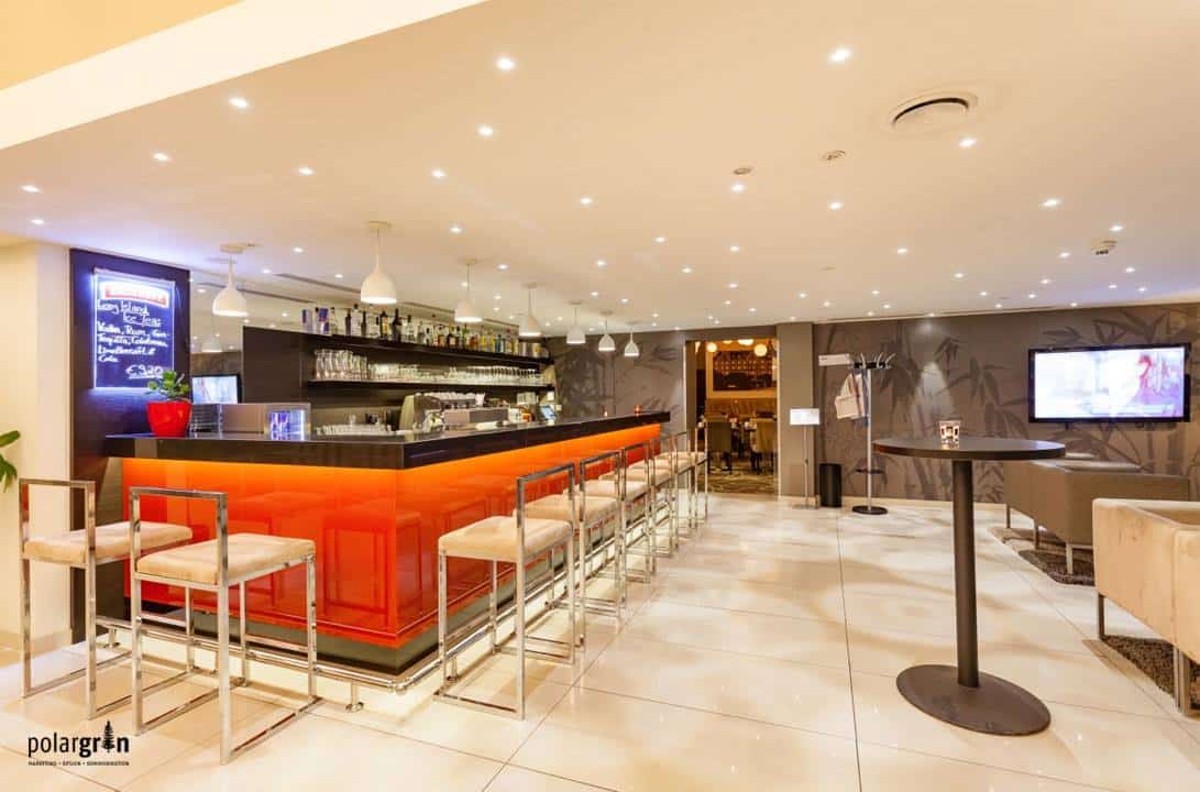 Hotelbar mit orange beleuchtetem Tresen und Barhockern