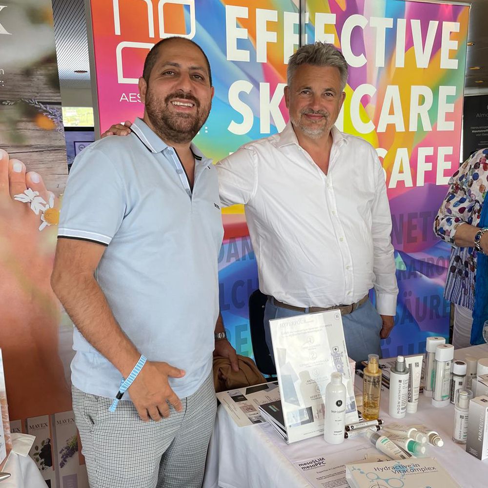 Zwei Männer vor der Produktwand von NOON Aesthetics auf einer Veranstaltung