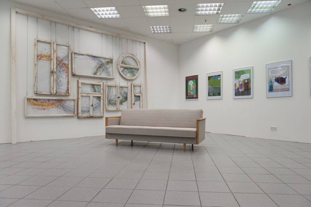 Ausstellungsraum mit Bilderwand und einem Sofa in der Mitte