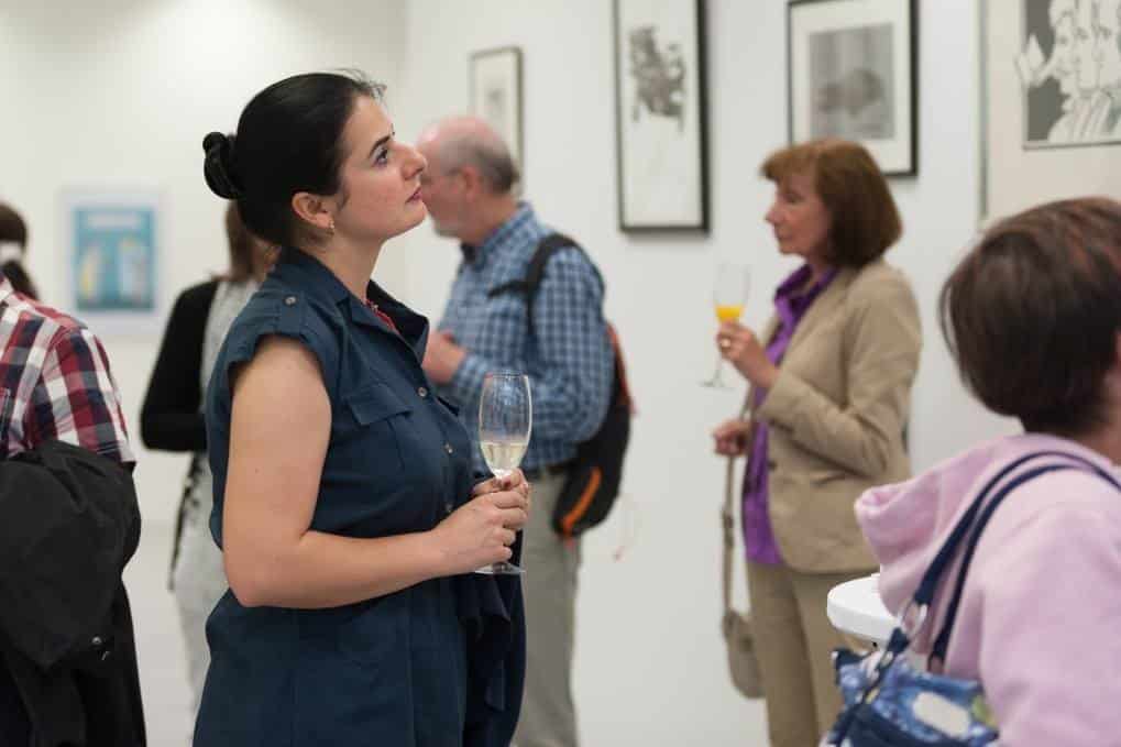 Besucherinnen und Besucher einer Vernissage im Gespräch, mit Gläsern in der Hand