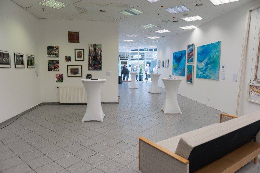 Ausstellungsraum mit gerahmten Bildern an den Wänden und Stehtischen